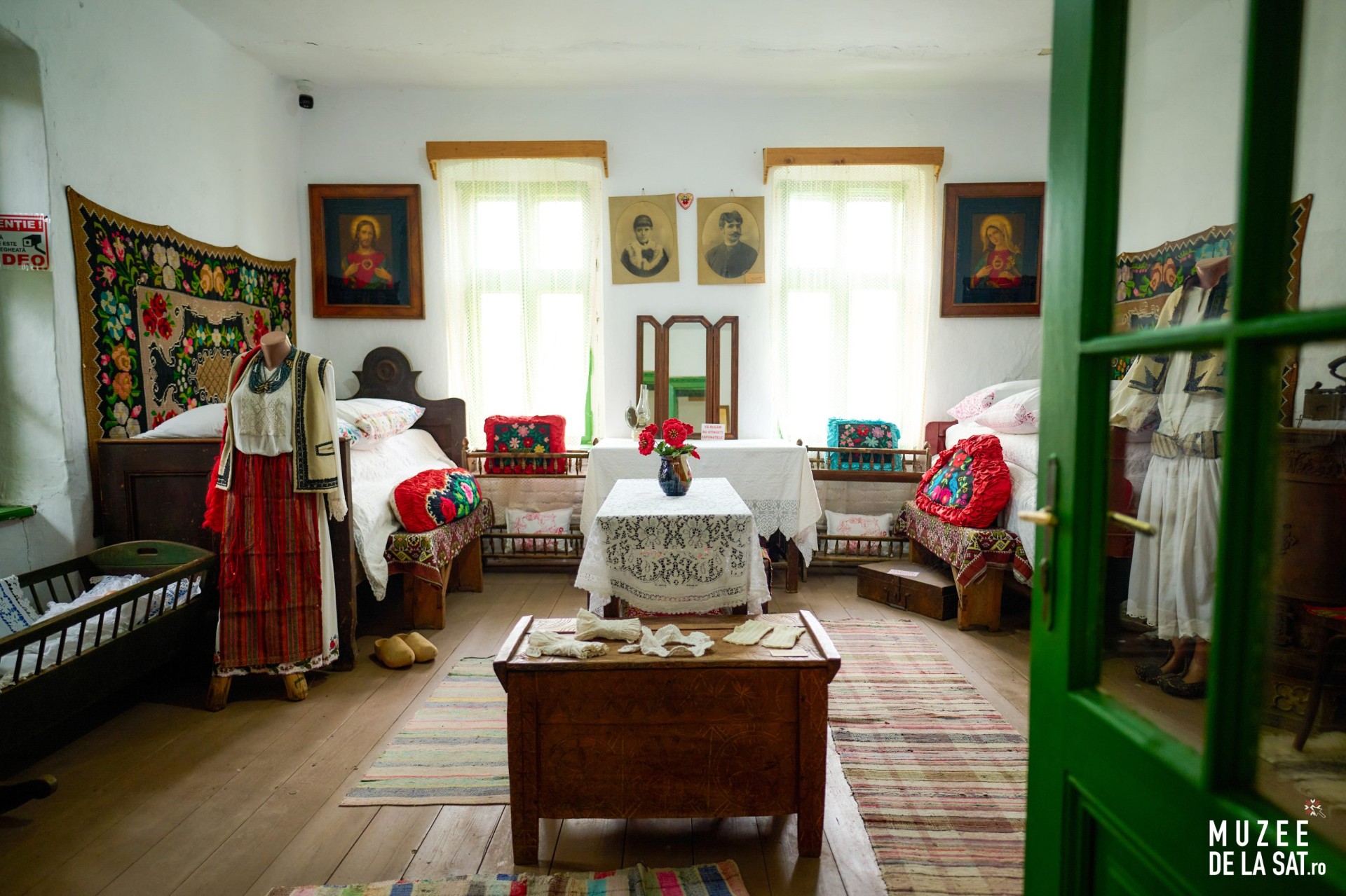 Cameră tradițională de muzeu cu costume populare, paturi îmbrăcate în textile și mobilier vechi